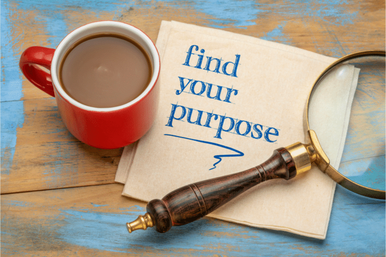 A coffee cup, a magnifier, and a piceof paper printed with "find your life purpose." They are all at a wooden table.