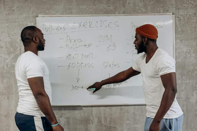 Two Men Looking At A Workout Schedule On A Whiteboard